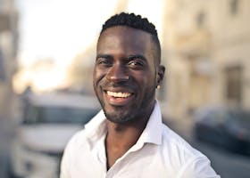 Portrait of a smiling man in a white shirt standing outdoors on a sunny day.
